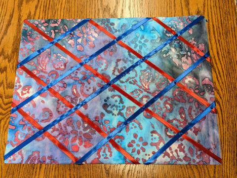 Memory board made with blue and red batik quilting cotton, blue and maroon ribbon, and blue map pins.