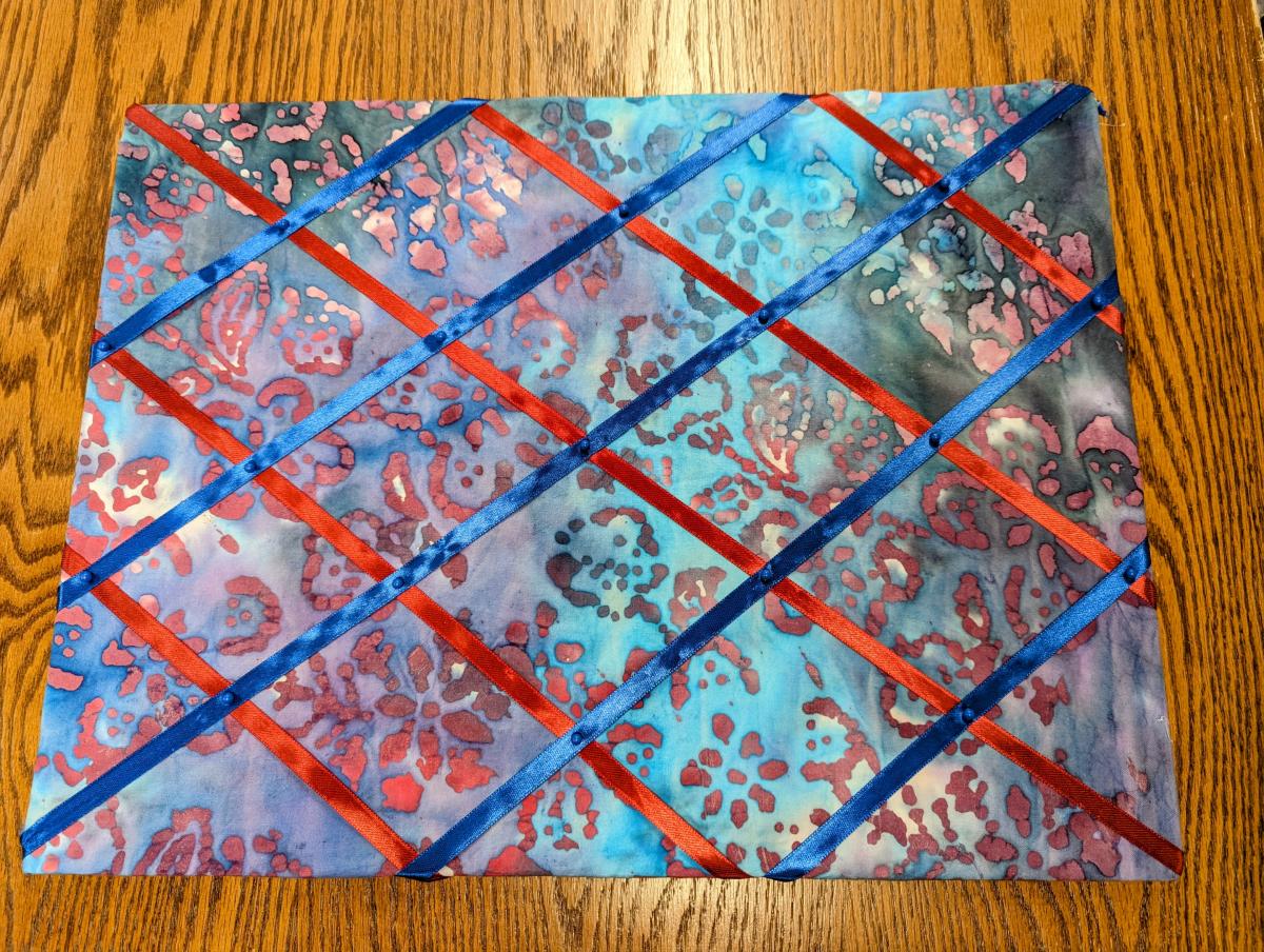 Memory board made with blue and red batik quilting cotton, blue and maroon ribbon, and blue map pins.