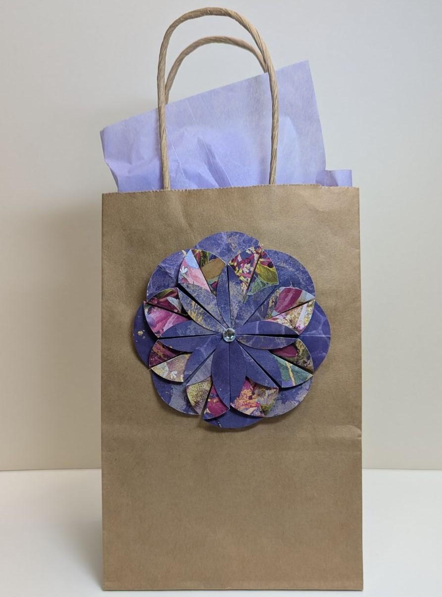 Small kraft gift bag with a colorful paper flower on the front.